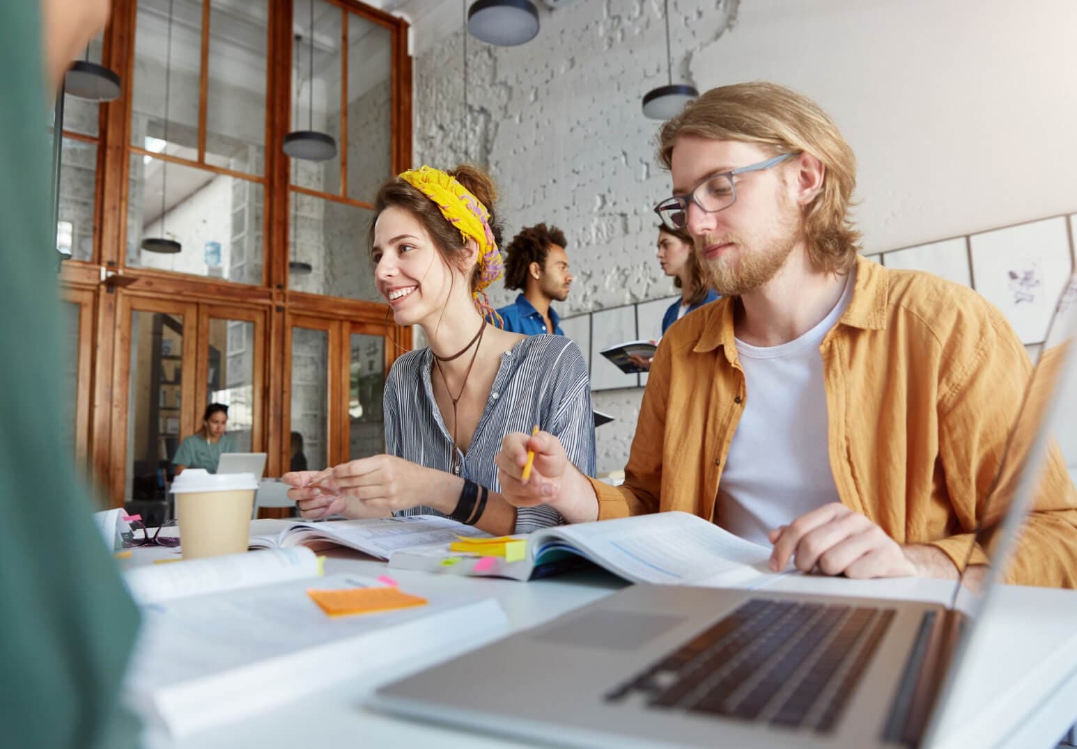 Two web designers working in an office with laptops while a person is walking in the background