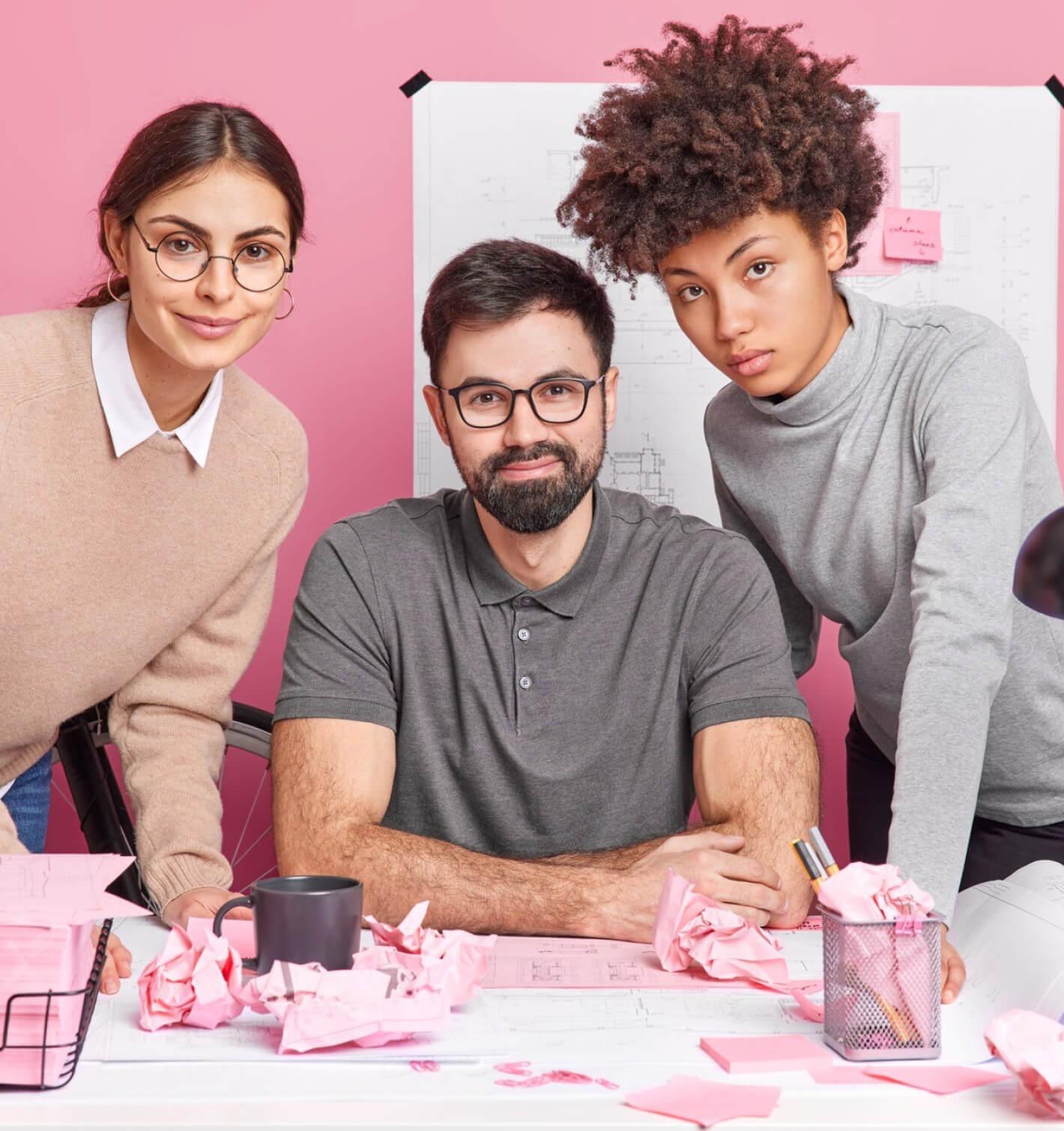 Three web designers working in an office with different expressions looking at the camera