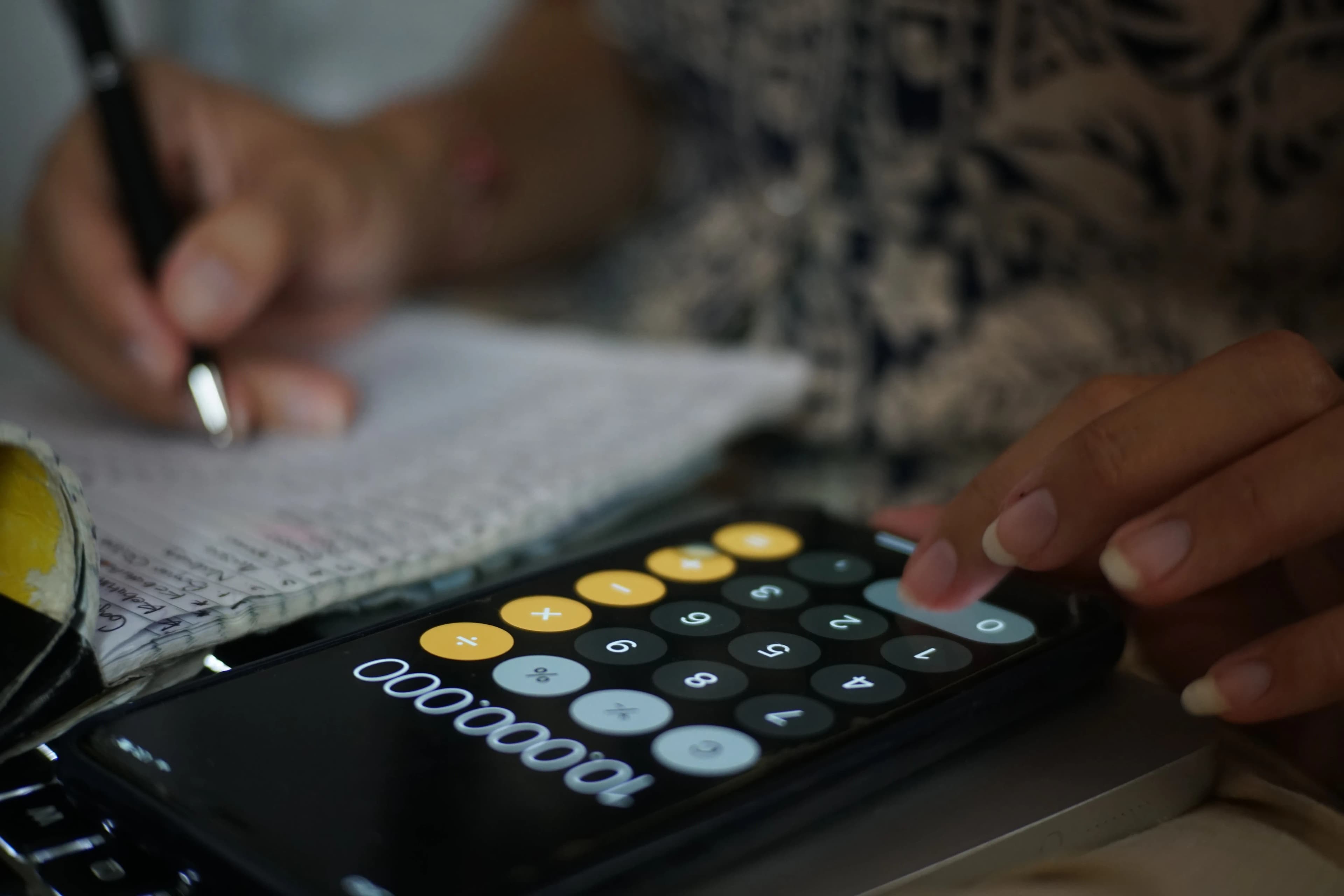 Woman using calculator on mobile with pen and paper to work our web design pricing
